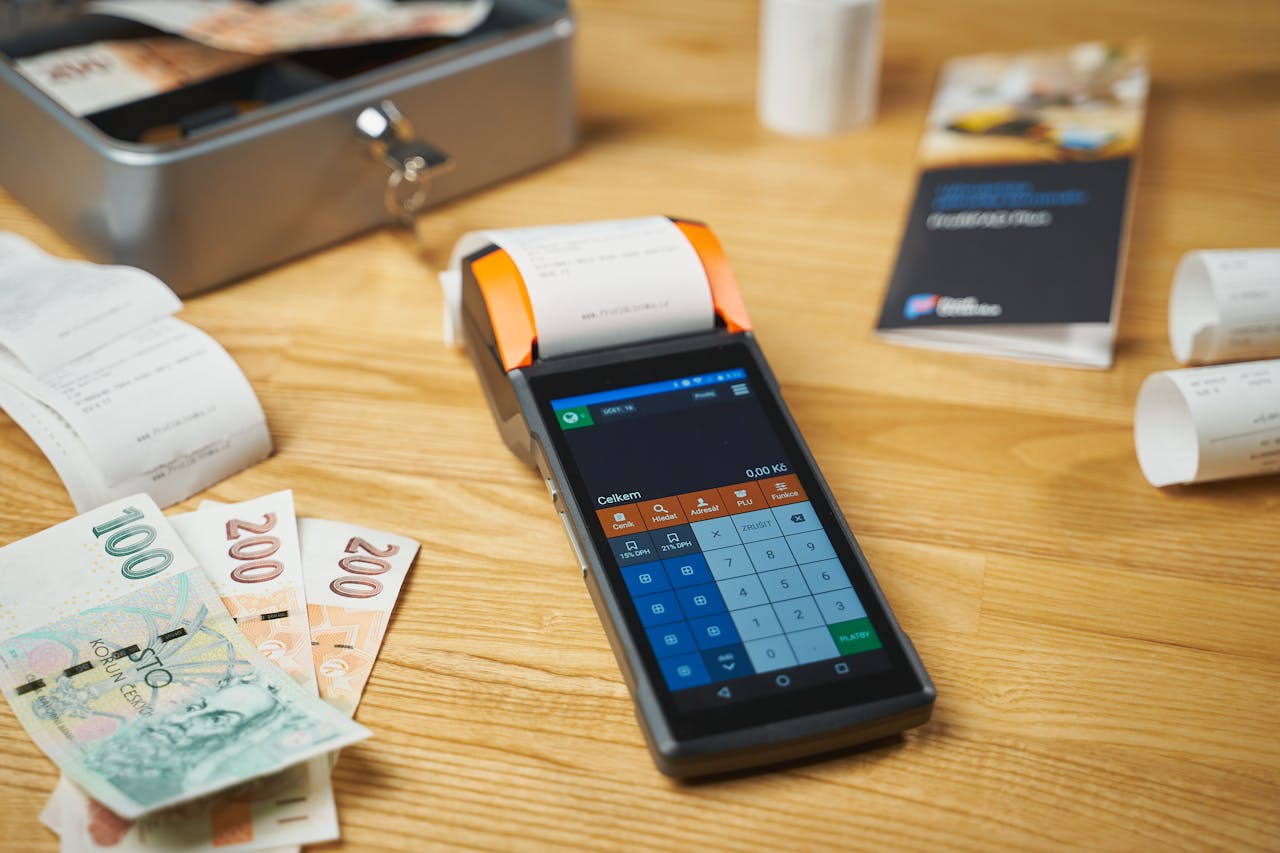 A modern digital payment terminal on a wooden desk with cash and receipts.